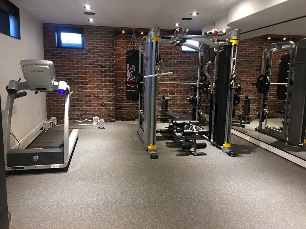 Indoor gym featuring a seamless light grey rubber floor, a treadmill, a weight machine, a UFC heavy bag, and an exposed brick wall.