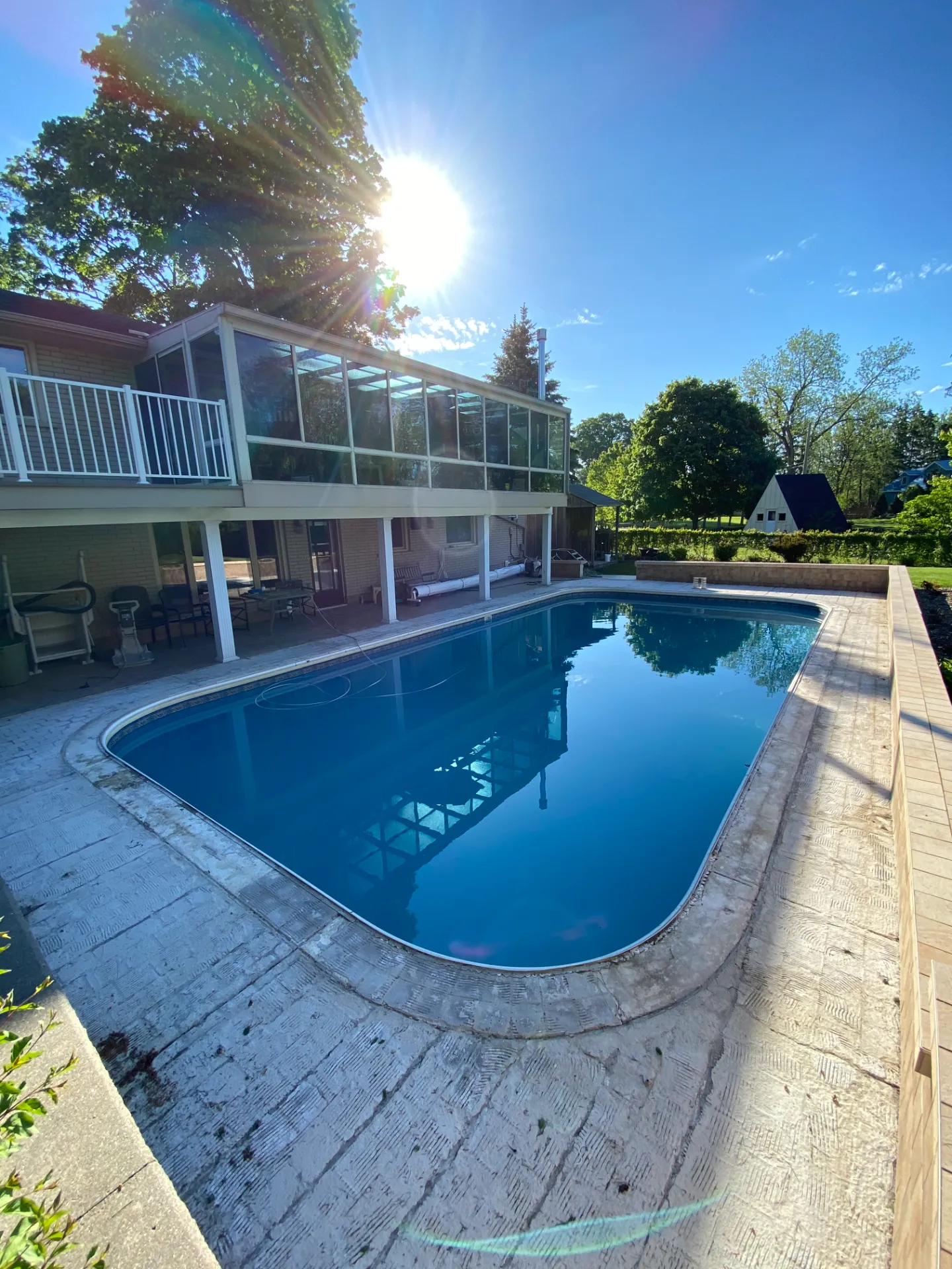 Pool deck before resurfacing: weathered stamped concrete around a rectangular pool, with a screened sunroom behind.