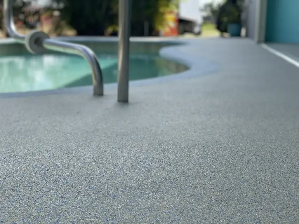 Close-up of a blue-grey Rubber Stone pool deck surface beside a pool ladder, with a curved concrete-free edge.