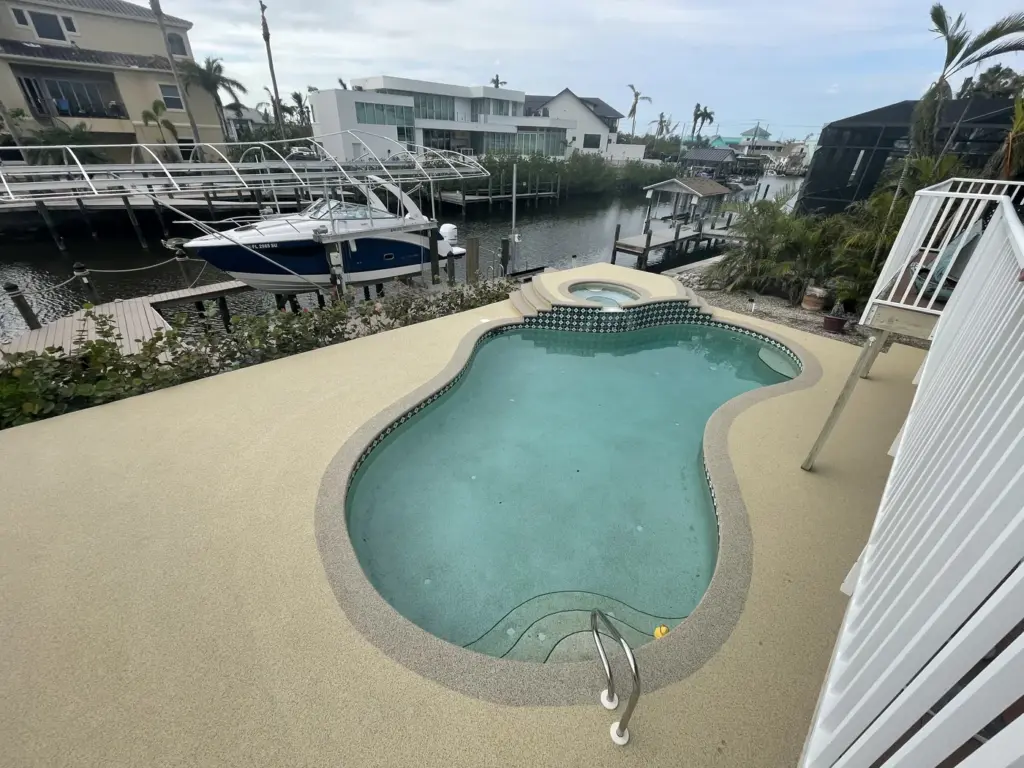 Resurfaced pool deck with a kidney-shaped pool beside a canal with moored boats.