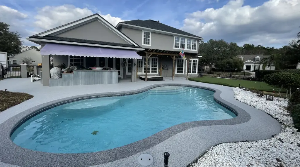 Freeform pool with a light resurfaced deck running up to a two-storey home