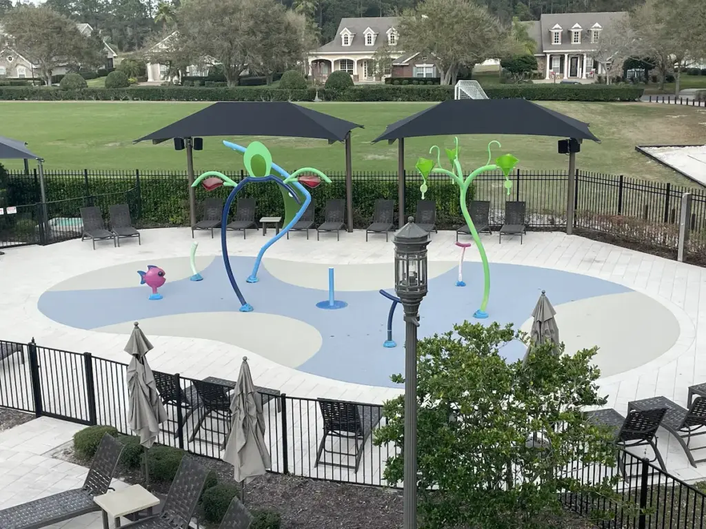 Splash pad in a public park with spray features, shade sails and a pale resurfaced deck.