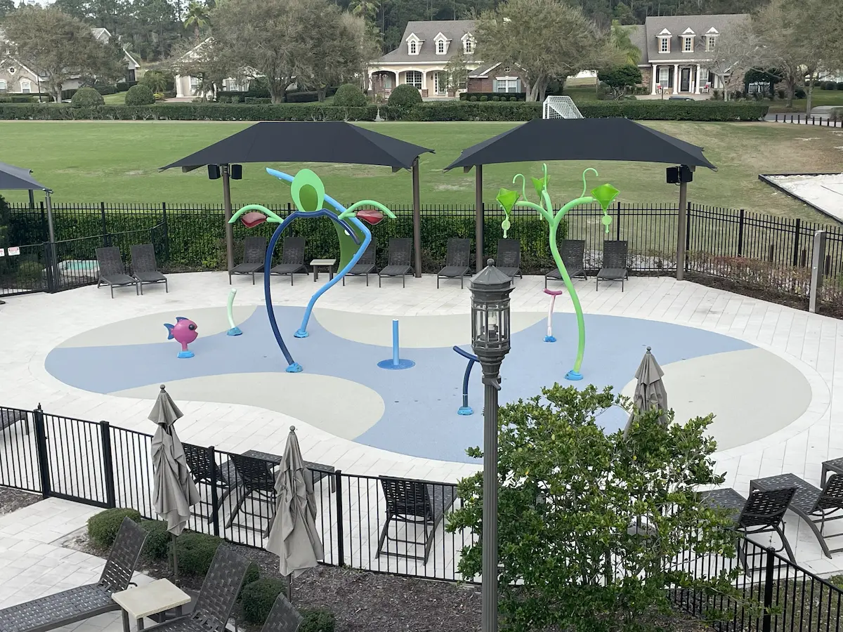 Splash pad in a public park with spray features, shade sails and a pale resurfaced deck.