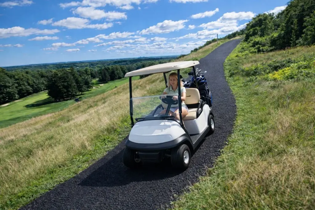 Golf cart driving along a bonded black rubber cart path through a golf course.