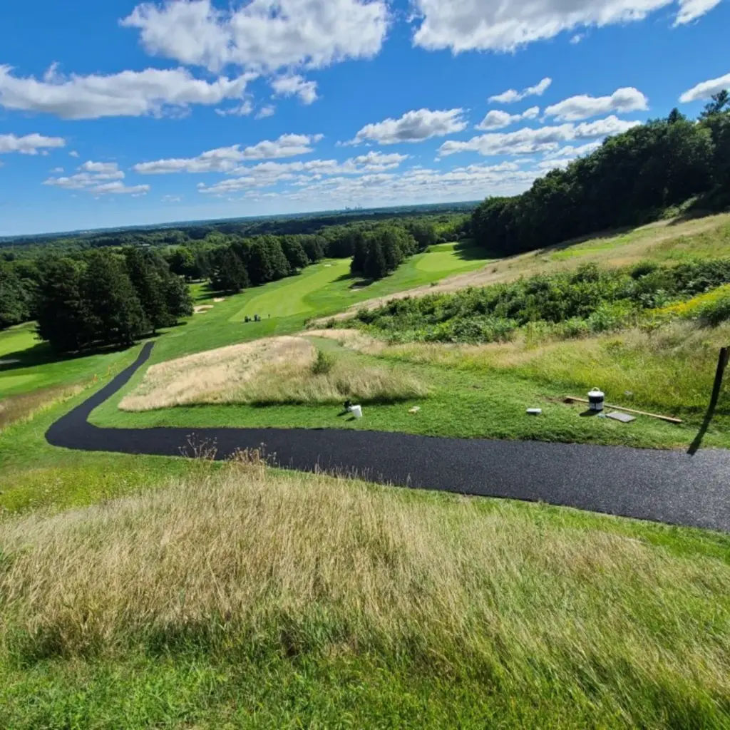 Aerial view of a black bonded rubber cart path curving across a golf course hillside.