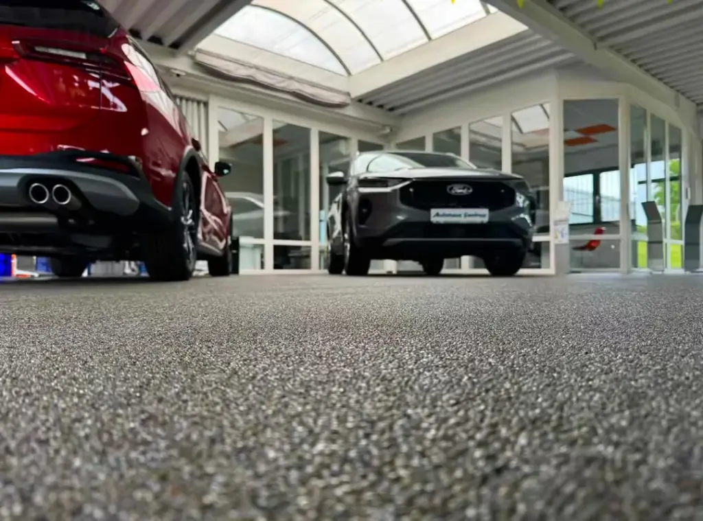 Close-up of a quartz natural stone floor in a car showroom, with vehicles in the background.